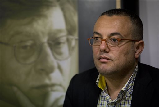 In this Sunday, March 1, 2015 photo, Palestinian novelist Atef Abu Saif sits next to a photo of late Palestinian poet and author Mahmoud Darwish, following a workshop discussing his novel, "A Suspended Life," in the West Bank city of Ramallah. Abu Saif, 41, who was shortlisted for a prestigious Arabic literature prize but couldn’t attend the ceremony because of alleged Hamas harassment says he learned story-telling from his refugee grandmother, who recounted happier times. AP 
