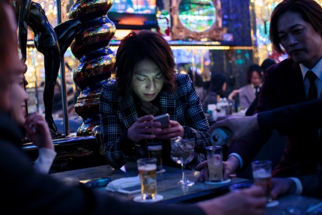 In this picture taken late on January 27, 2017, a male host checks his phone as he sits with other hosts and a female customer at a host club in the Kabukicho red-light district in Tokyo. Host clubs are a 10 billion USD industry in Japan with some 800 venues nationwide. Around 260 of those are located in Tokyo, most squeezed into Kabukicho's narrow streets where flickering neon signs display the air-brushed faces of hosts outside clubs with names such as Romeo, Gatsby and Avalon.  / AFP PHOTO / BEHROUZ MEHRI / TO GO WITH Japan-culture-lifestyle-hosts,FEATURE by Alastair HIMMER