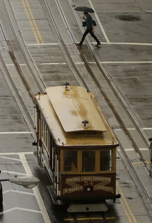 FILE-A cable car drives down California Street in front of a man carrying an umbrella in San Francisco, Thursday, Dec. 4, 2014.  AP