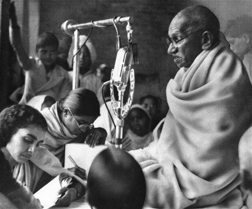 In a Jan. 22, 1948 file photo, Mohandas K. Gandhi squats before a microphone in New Delhi, India, to deliver prayer meeting discourse during second day of his fast to force communal peace in India. New England Brewing Co. in Connecticut is apologizing to Indians offended that the company is using Mohandas Gandhi's name and likeness on one of its beers. AP