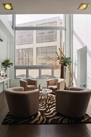 DOUBLE-VOLUME living room makes a narrow area seem larger. Glass wall maximizes natural light. Georgian leather armchairs match the rug’s wavy pattern.
