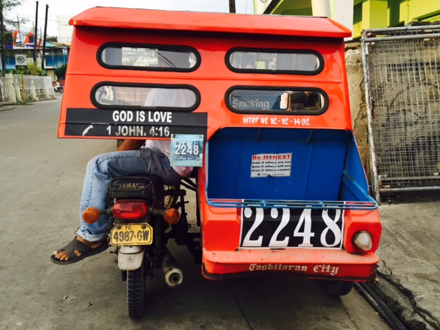 A tricycle in the city with a Biblical verse on its back: "God is love," from 1 John 4:8