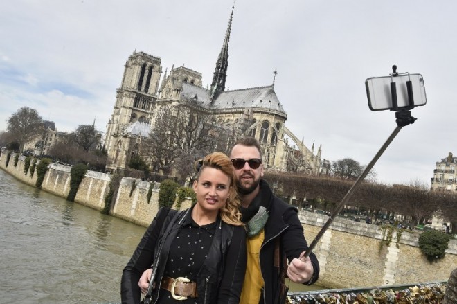 (FILES) This March 7, 2015 file photo shows tourists as they use a selfie-stick to take a picture of themselves near the Notre Dame cathedral in Paris.  Disney on June 26, 2015 became the latest major tourism operator to ban selfie sticks as part of a growing backlash against the extendable devices. The ban covers Disney theme parks in the United States, Paris and Hong Kong.  "We strive to provide a great experience for the entire family, and unfortunately selfie sticks have become a growing safety concern for both our guests and cast," said Kim Prunty, a Disney spokeswoman. AFP PHOTO