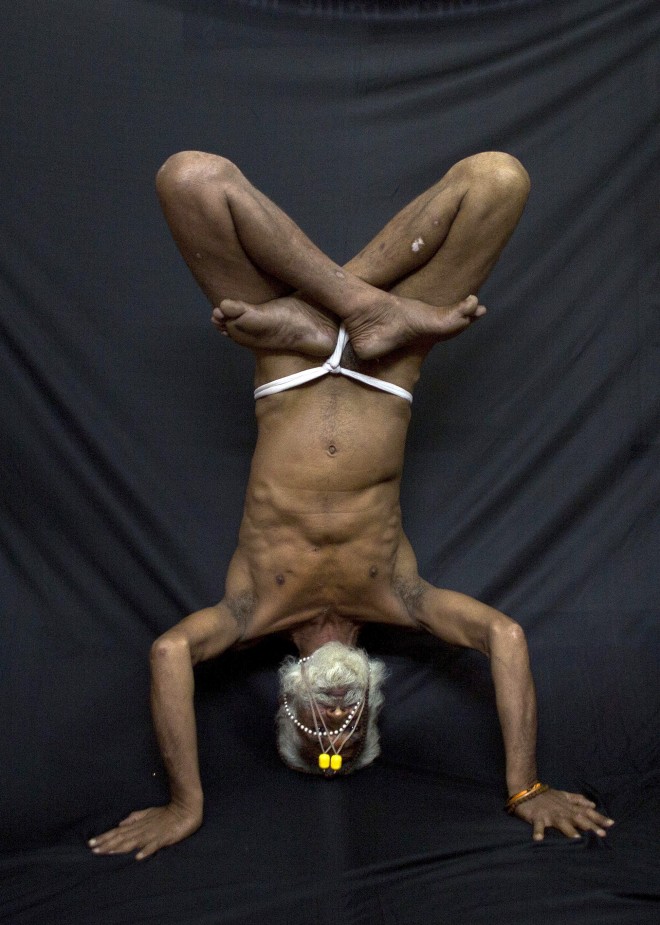 In this Friday, June 12, 2015 photo, an Indian Hindu holy man, illustrates the yoga pose Ardha Sirasana, where the yogi lies on his back and puts his crossed legs in the air, in Gauhati, India. Sunday marks the first International Yoga Day, which the government of India Prime Minister Narendra Modi is marking with a massive outdoor New Delhi gathering. (AP Photo/Anupam Nath)