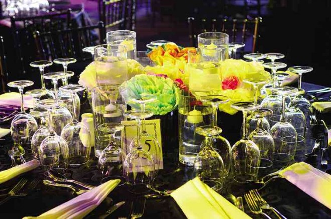 TABLE setting of bright colored paper flowers against black table cloth and glittering votive candles