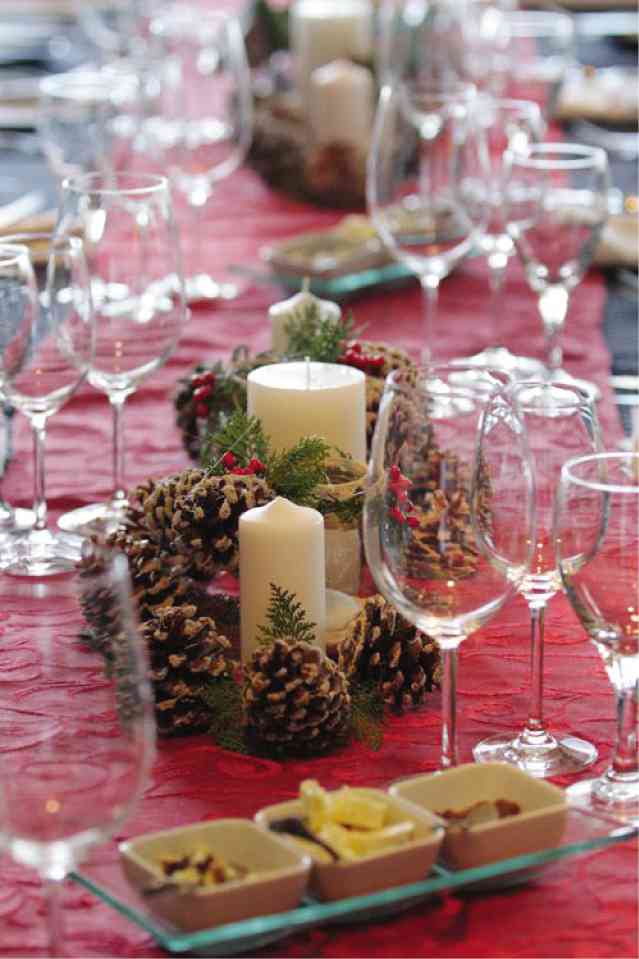 HOLIDAY setup pairs pine cones and pillar candles with clear glass and a red tablecloth.