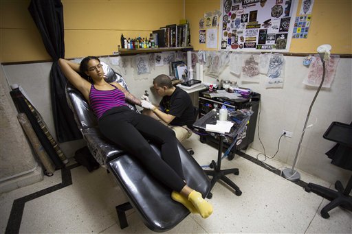 In this Feb. 5, 2016 photo, tattoo artist Mauro Coca works on a drawing of a tropical bird on the arm of 21-year-old Julivic Marquez, from the the Dominican Republic, at La Marca, or The Brand tattoo parlor in Havana, Cuba. Skin art is on the rebound in Cuba, with hundreds of tattoo parlors operating across the country. The socialist revolution drove tattooing underground, with health inspectors and police raiding studios seen as health hazards and vestiges of capitalist immorality. (AP Photo/Desmond Boylan)