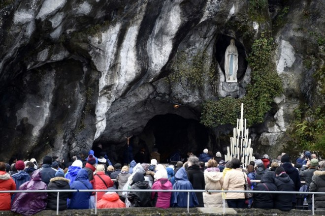 Pilgrim gather under the statue of the Virgin Mary inside the Massabielle grotto on February 11, 2016 for the 158th anniversary of the virgin Mary's apparition to Bernadette Soubirous in Lourdes, Southern France. AFP PHOTO