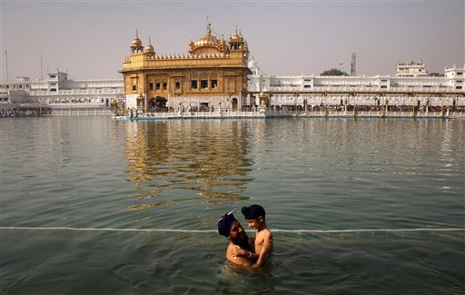 In this April 13, 2013, file photo, a Sikh man holds a child as they take a holy dip in the sacred pond at the Golden Temple, Sikhs holiest shrine, during Baisakhi festival in Amritsar, India. The chronic air pollution blanketing much of northern India is now threatening the holiest shrine in the Sikh religion, making the once-gleaming walls of the Golden Temple dingy and dull. (AP Photo/Sanjeev Syal, File)