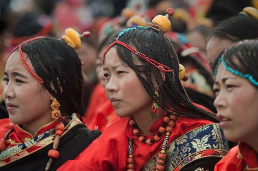 In this picture taken on July 26, 2016 ethnic Tibetans wearing traditional costumes and jewellery, watch a fashion show at a local government sponsored festival in Yushu, in the northwestern Chinese province of Qinghai. The festival held since the 1990s lasts for around five days. It was suspended for several years following a 2010 earthquake in Yushu which killed some 2,700 people. / AFP PHOTO / NICOLAS ASFOURI