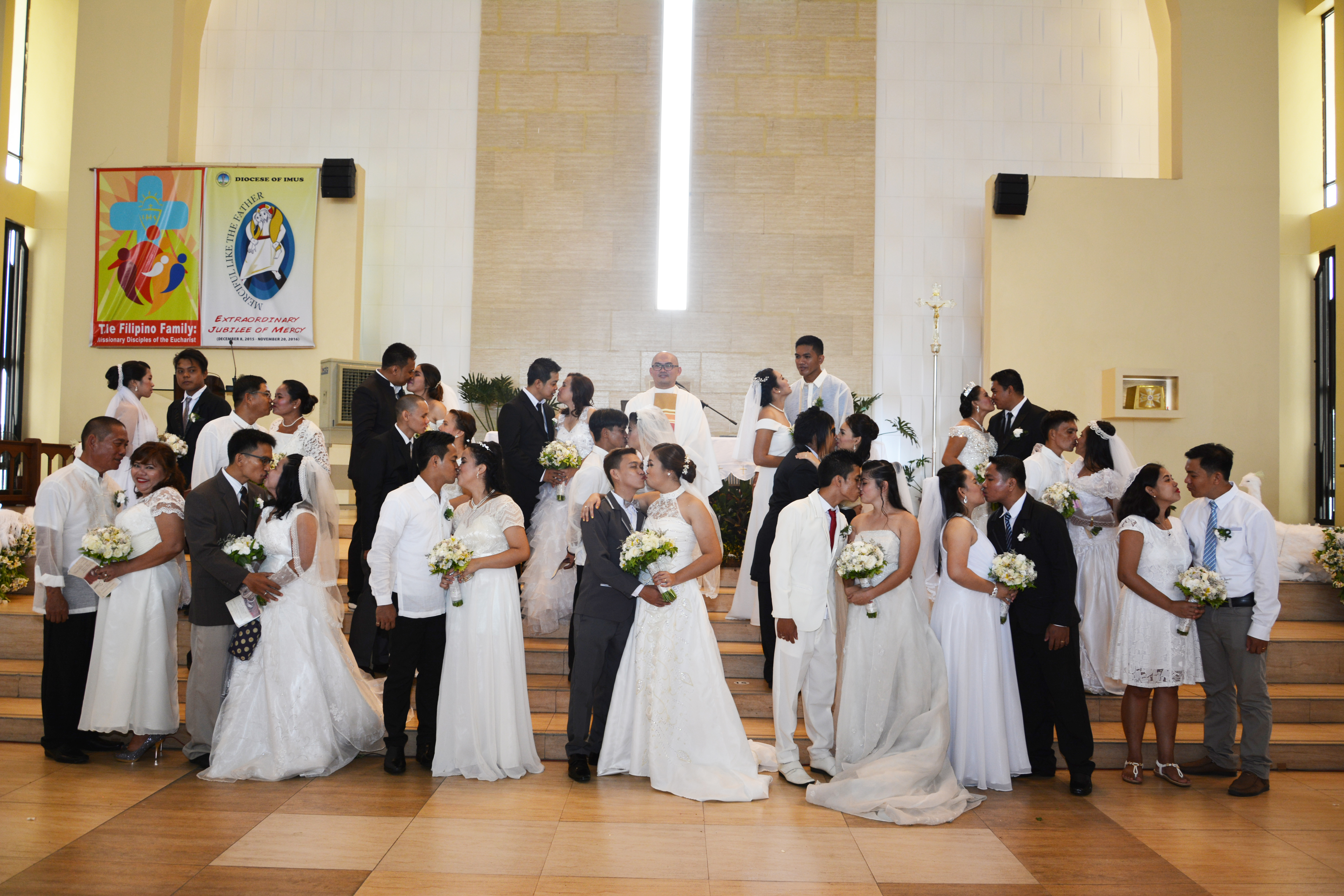 A group shot of the seventeen May Forever: Kasalan sa Lancaster New City couples celebrating a successful wedding at the Church of the Holy Family