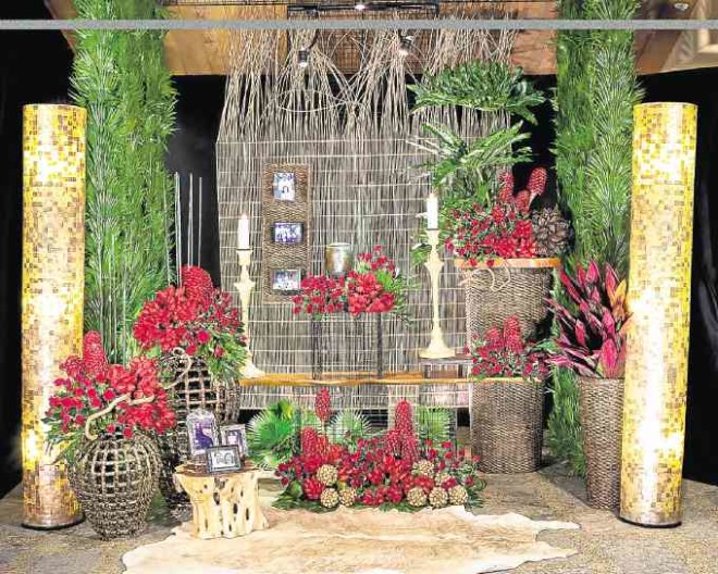Red flowers represent a celebration of love brought into the next life. The setting is adorned with a rattan divider, “capiz” floor lamps, rattan buds, tree stump with photos and carved candelabras.