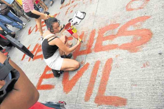 ‘HERE LIES EVIL’. Awoman protester paints her sentiments near the gates of Libingan ng Mga Bayani. —MIKE NAVALLO