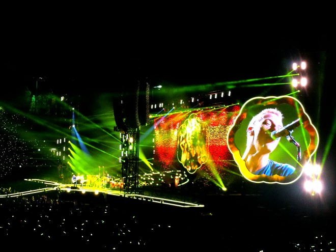 The Coldplay stage has a kaleidoscope backdrop including a cloud-shaped video screen.