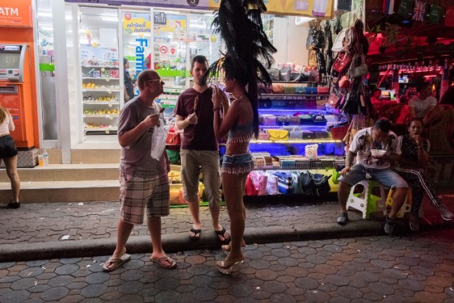 This photo taken on March 29, 2017 shows two foreign tourists (L) standing in front of a stall selling handbags in Walking Street in Pattaya. Two hours east of Bangkok, Pattaya's bawdy reputation hails from the Vietnam War era when US GIs partied in their downtime. / AFP PHOTO / Roberto SCHMIDT / TO GO WITH Thailand tourism crime social,FEATURE by Jerome TAYLOR