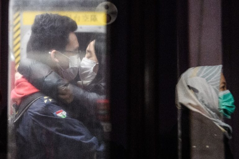 A couple wearing face masks kiss on an underground metro train as another passenger (R) is reflected on a platform glass door during a Lunar New Year of the Rat public holiday in Hong Kong on January 27, 2020, as a preventative measure following a coronavirus outbreak which began in the Chinese city of Wuhan. (Photo by Anthony WALLACE / AFP)