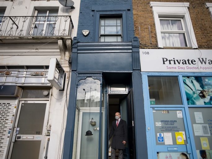 Estate agent David Myers stands in the doorway of what is dubbed 'London's thinnest house' (painted blue) in west London on February 5, 2021. - Wedged neatly between a doctor's surgery and a shuttered hairdressing salon, the five floor house in Shepherds Bush is just 5ft 6ins (1.6 metres) at its narrowest point and is currently on the market for £950,000 ($1,300,000, 1,100,000 euros). The unusual property, originally a Victorian hat shop with storage for merchandise and living quarters on its upper floors, was built sometime in the late 19th or early 20th century. (Photo by Tolga Akmen / AFP)