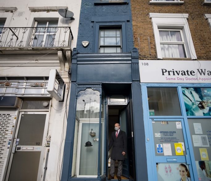 Estate agent David Myers stands in the doorway of what is dubbed 'London's thinnest house' (painted blue) in west London on February 5, 2021. - Wedged neatly between a doctor's surgery and a shuttered hairdressing salon, the five floor house in Shepherds Bush is just 5ft 6ins (1.6 metres) at its narrowest point and is currently on the market for £950,000 ($1,300,000, 1,100,000 euros). The unusual property, originally a Victorian hat shop with storage for merchandise and living quarters on its upper floors, was built sometime in the late 19th or early 20th century. (Photo by Tolga Akmen / AFP)