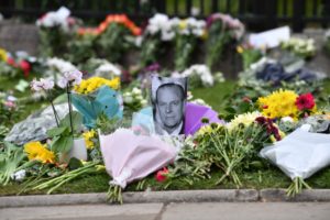A photograph of Britain's Prince Philip, Duke of Edinburgh is positioned among floral tributes outside Windsor Castle in Windsor, west of London, on April 10, 2021, the day after the duke's death at the age of 99. - Military guns will be fired across Britain and sporting events will fall silent on Saturday as part of worldwide tributes to mark the death of Queen Elizabeth II's husband, Prince Philip