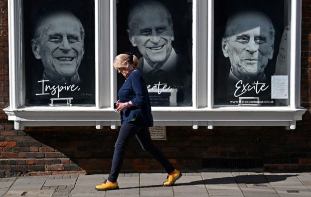 A pedestrian walks past a shop displaying images of Britain's Prince Philip, Duke of Edinburgh, in Windsor, west of London, on April 13, 2021, following his death on April 9, at the age of 99. - Princes William and Harry on Monday issued emotional tributes to their grandfather Prince Philip, whose death on April 9, aged 99, has thrown the younger men together for the first time since an explosive row engulfed the family