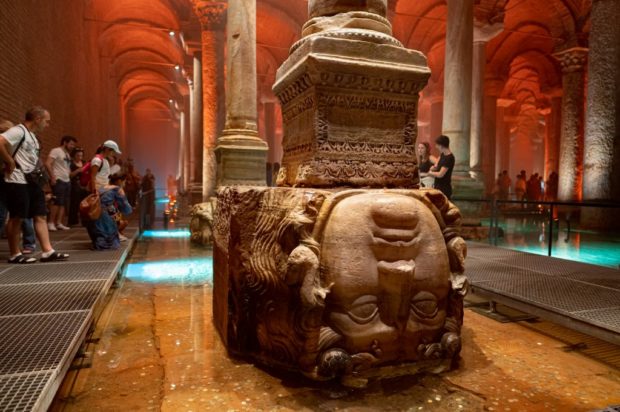 People stands next to the Medusa head in the Basilica Cistern while visiting the historic site in Istanbul, Turkey, on July 26, 2022.