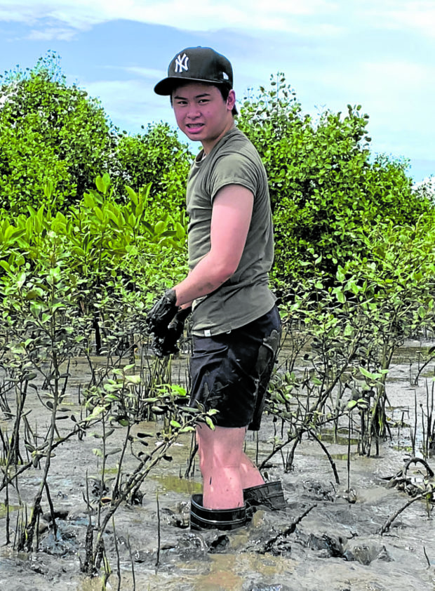 Tyler Uy standing knee-deep in mud with the 8-month-old mangrove trees he planted