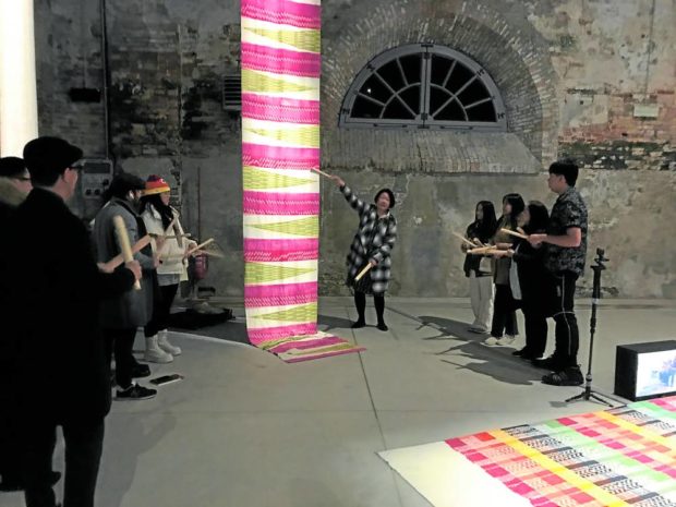 Prudente leads a group of volunteers in using “kaluntang” (sticks made from “palotsina”) to perform the woven textile score on the last day of the Biennale.