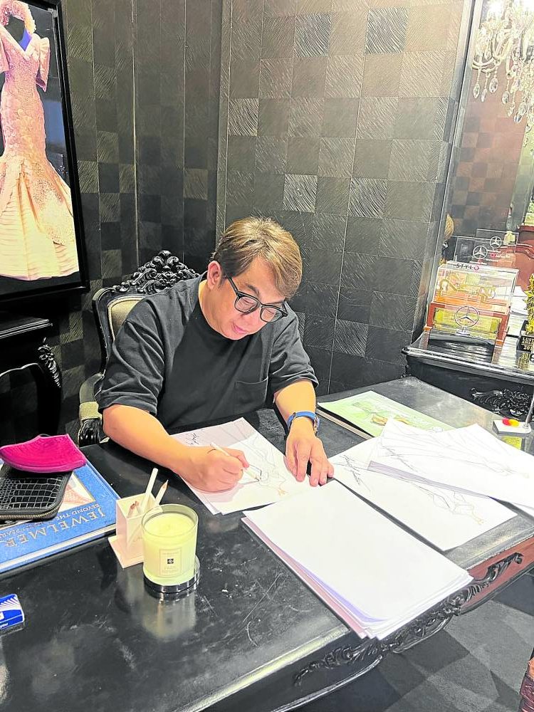 Andrada draws on his desk.  Partially seen to the left is the national costume he designed for Wurtzbach inspired by the queens of Manila's carnival.