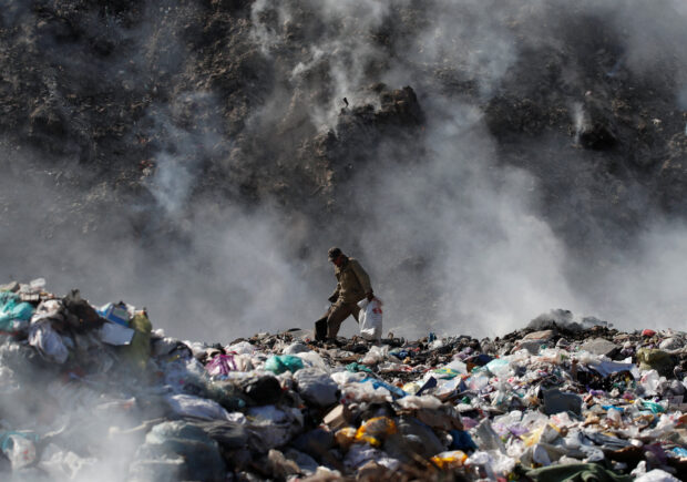 A man searches for recyclable materials as smoke billows from burning garbage at a landfill in the outskirts of Bishkek