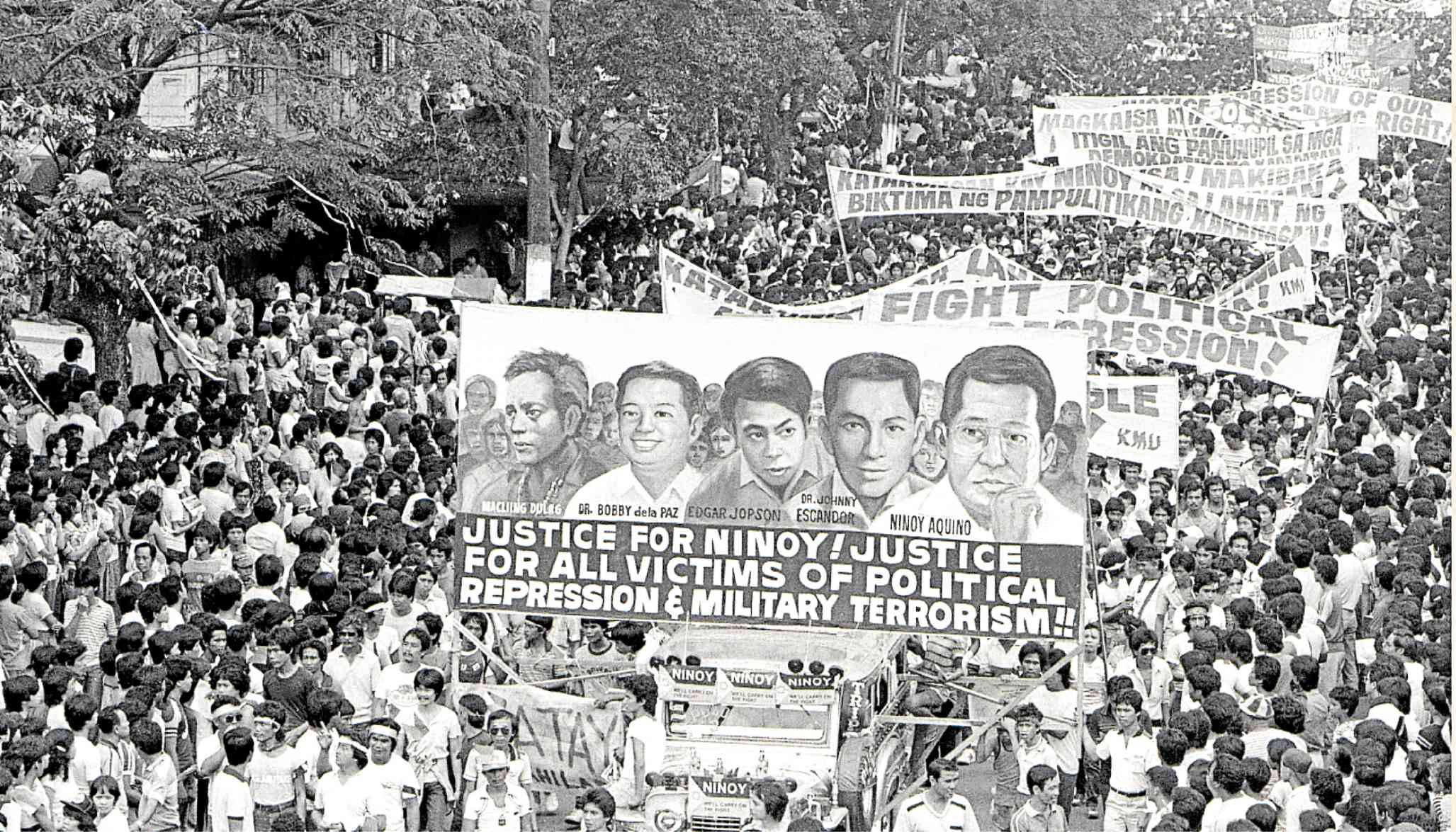 Thousands of demonstrators march to Quirino Grandstandwith a banner calling for justice for Macli-ing Dulag, Dr. Bobby dela Paz, Edgar Jopson, Dr. Johhny Escandor and Ninoy in April 1984.