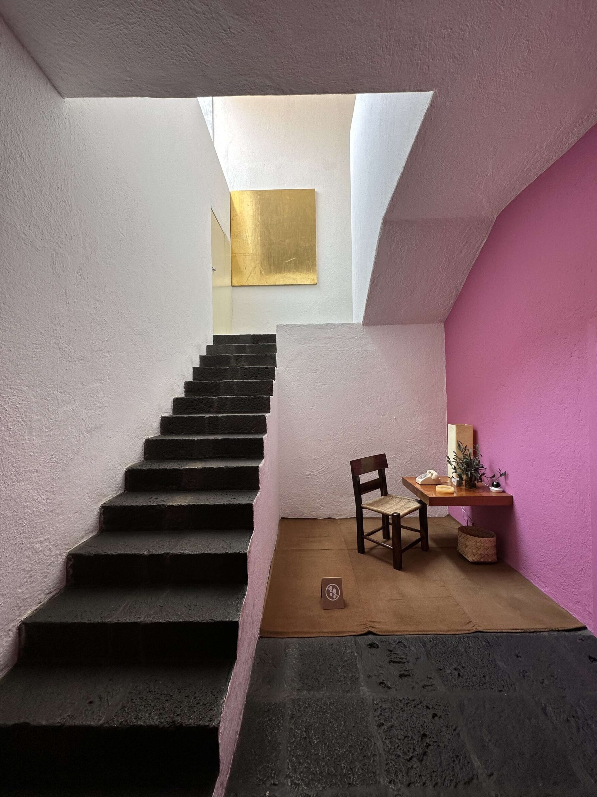 The vestibule inside Casa Luis Barragán, with the steps and floor built out of raw volcanic stone, where white and black are contrasted by the pink walls