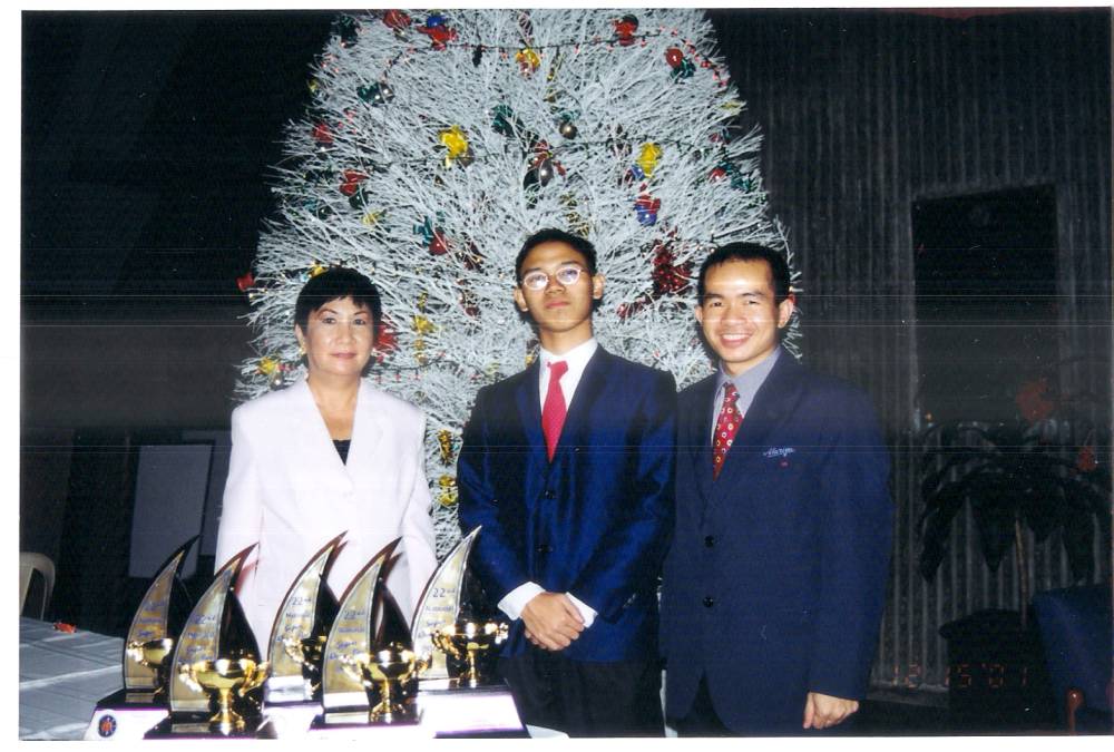 The author (center) with Gloria “Gay” Palarca Tayag, president and cofounder, Quiz Bee Foundation, and Percival Almoro, one of the author’s coaches, with the trophies. He also won an en- cyclopedia set and other books, gift packages from corporate sponsors, and a desktop computer.